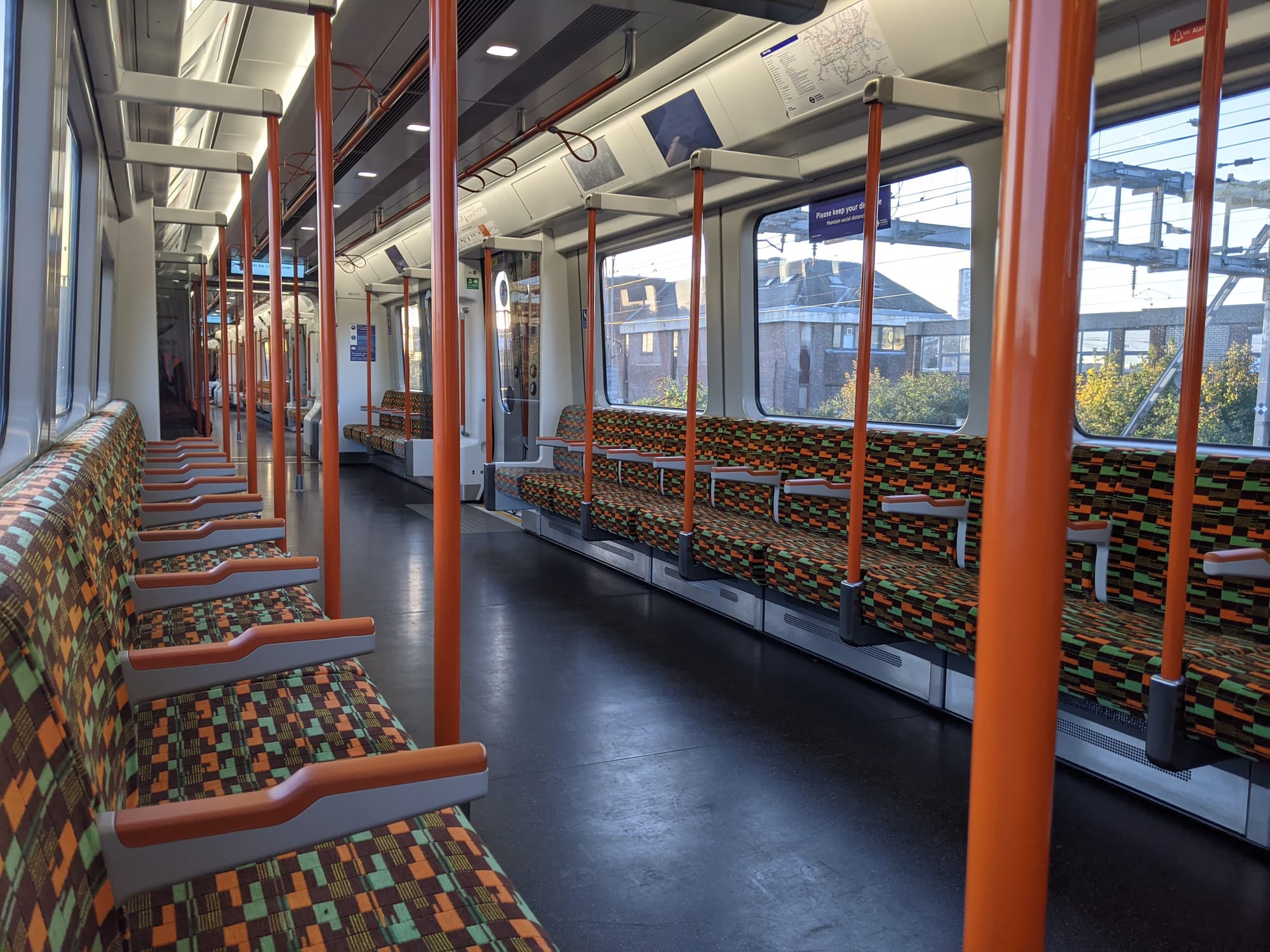 Seats are positioned along the outside of the carriage with a spacious walkway. There are bright orange handles and grab handles for standing passengers. The train is connected by continuous gangways, meaning there are no doors between carriages.