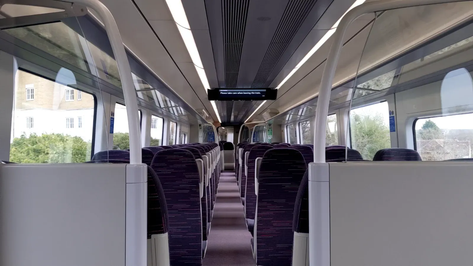 Sets of two seats are seen on the left and sets of three seats are seen on the right, leaving a narrow path between them. On the seats are grey grab handles.