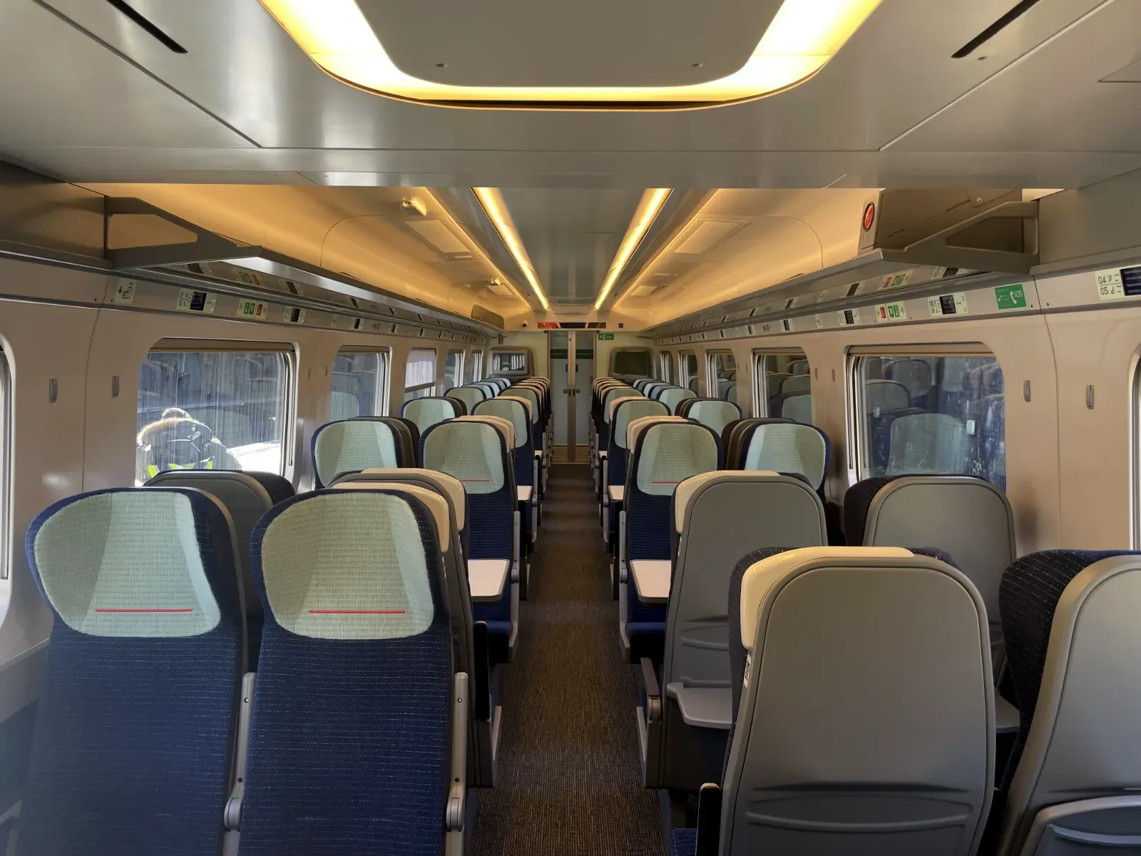 The interior of Avanti's class 805 with rows of modern seating and dark blue upholstery with light blue head rests. There are overhead luggage racks and large windows on both sides. There are white grab handles along the edges of the seats.