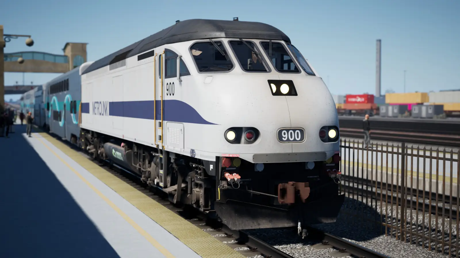 A diesel Metrolink locomotive is stationery at San Bernardino under clear, blue skies. In the background are freight cars awaiting hauling.