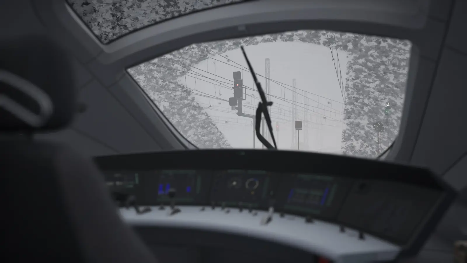 A view of the train controls over the shoulder of the driver's seat. It is stormy outside, and the cab window has been covered by snow.