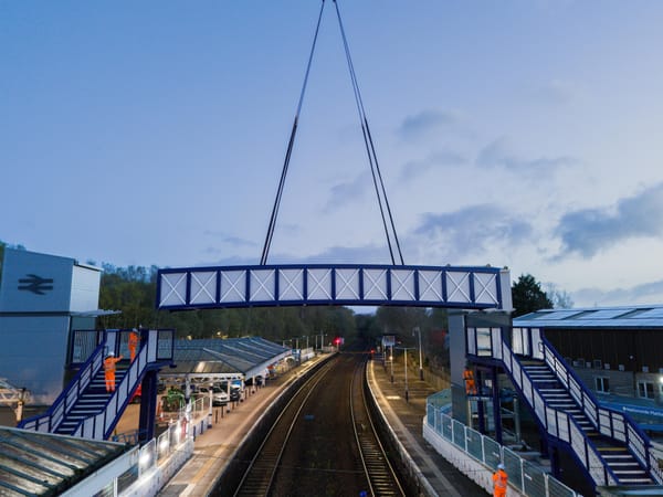 A blue and white footbridge is lowered by a crane (out of frame) between two sets of stairs.