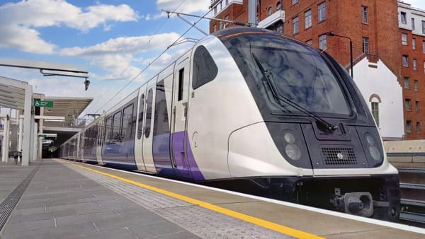 A Class 345 Elizabeth line train, with a purple and white livery, approaches a station.