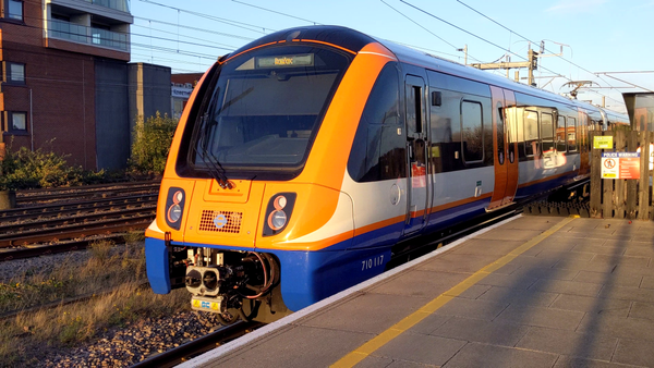 A train approaches a platform. The front of the train is a bright orange, as are the doors on the carriage.