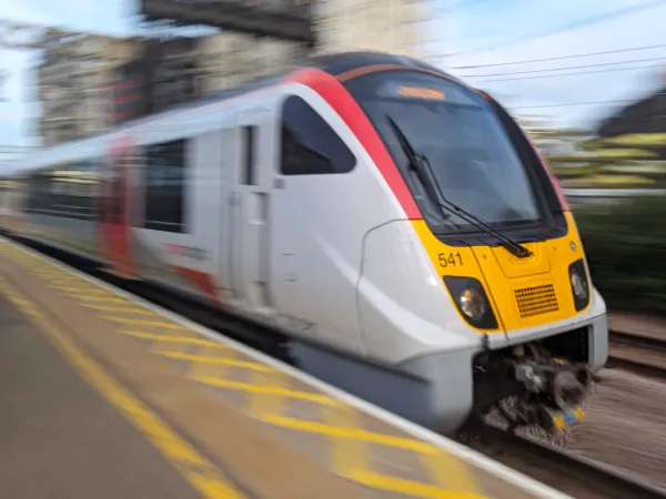 A commuter passenger train with a red and white exterior is captured in motion as it passes through Stratford in London.