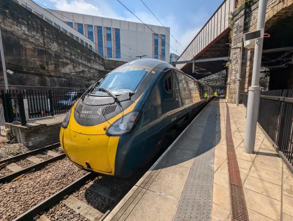 A Class 390 electric train is stationery at Liverpool Lime Street. It has a yellow front and turquoise and white livery.