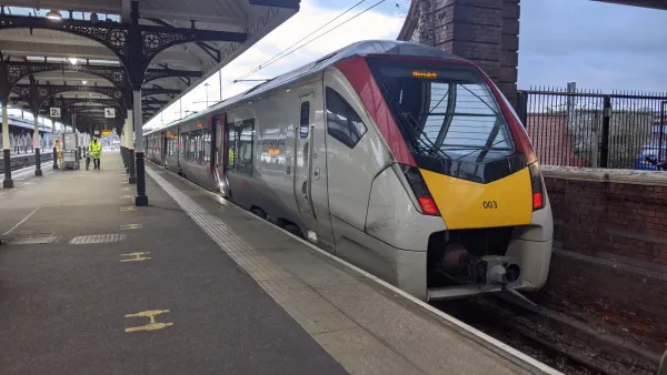 A Class 745 train is stationary at Norwich station. The front is yellow and red. It is in a white Greater Anglia livery.