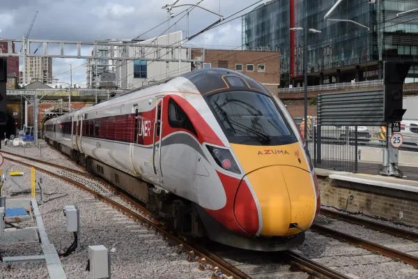 A modern LNER Azuma train on a track near King's Cross, surrounded by buildings and overhead electric wires.