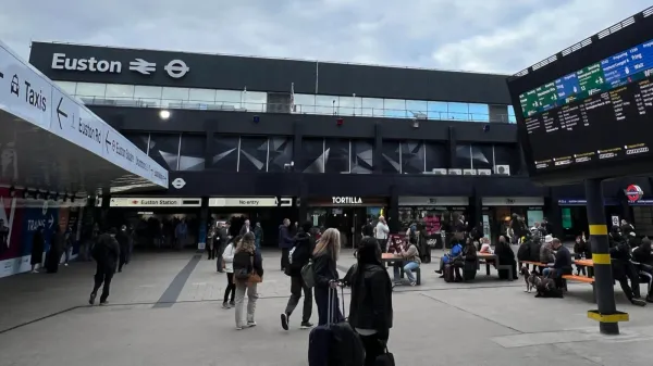 London Euston exterior: a wide, black building with shops along the front, passengers watching the departure board.