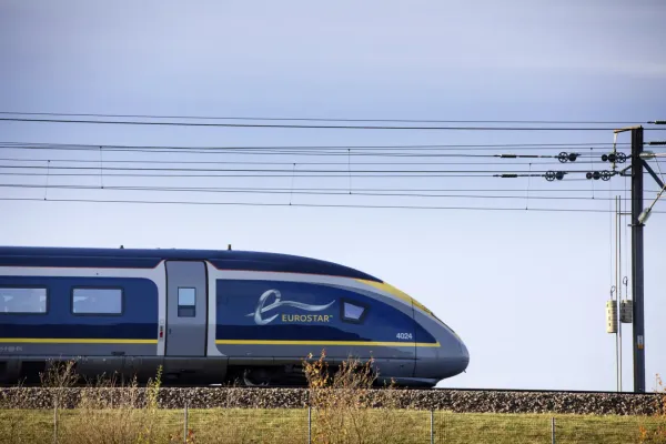 A Eurostar train in its navy blue livery, accented by yellow, speeds through the countryside under clear, blue skies.