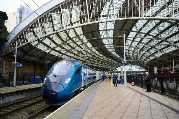 An Avanti West Coast train on a platform under a large, arched glass roof, with passengers waiting nearby.