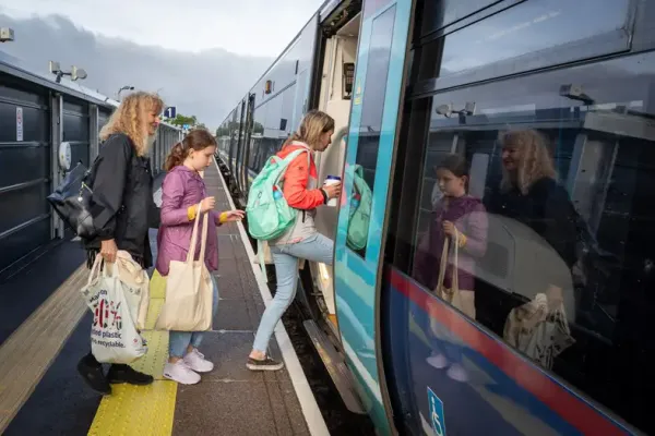 Three passengers carrying tote bags board a Southeastern train with a navy and sky blue livery.