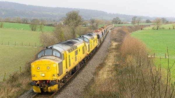 Coupled diesel locomotives painted bright yellow haul liquid tankers along the single-track Cambrian line.