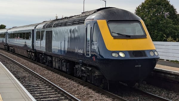 A ScotRail intercity train waits next to a platform to depart. Its livery includes silhouettes of Scottish landmarks.