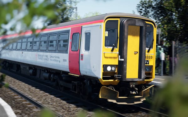 A Class 153 train in Transport for Wales white and red livery is captured in the background behind some foliage.
